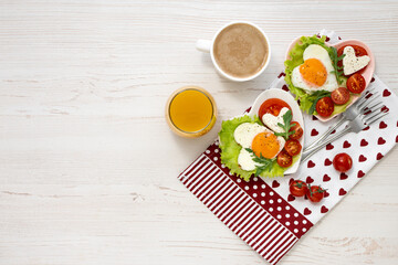 Nicely served breakfast on Valentine's Day. Two heart-shaped plates with fried eggs, tomatoes and cheese, coffee and juice on a white wooden table. View from above. Banner. Healthy breakfast.