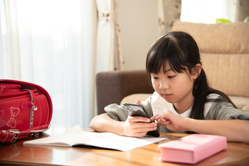 宿題をやらないでスマホを見る小学生の女の子