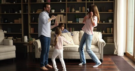 Vivacious family with kids dancing in living room, full length view. Happy homeowners celebrate relocation day to new own first house, enjoy life event and holidays. Bank loan, weekend leisure concept