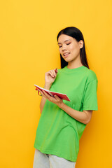 woman with Asian appearance green T-shirts with red notebook and pen yellow background unaltered