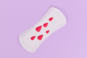 Female period concept with panty liner with symbolic paper blood drops on pink background with copy space