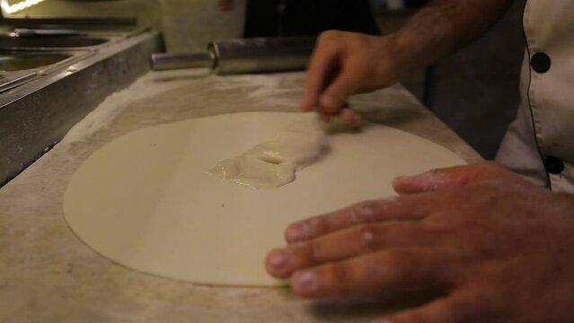 The chef prepares the pizza dough. Spread the sauce with a brush, something like a painting. Cooking is an art.