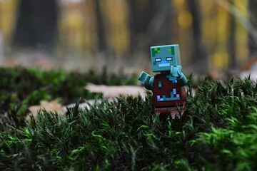 Obraz premium LEGO Minecraft hostile Drowned Zombie mob walking with raised hands on wet moss surface in real world autumn forest