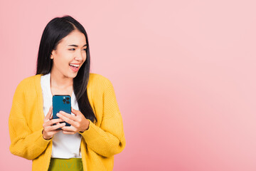 Happy Asian portrait beautiful cute young woman teen smiling excited using smart mobile phone studio shot isolated on pink background, Thai female surprised making winner gesture on smartphone