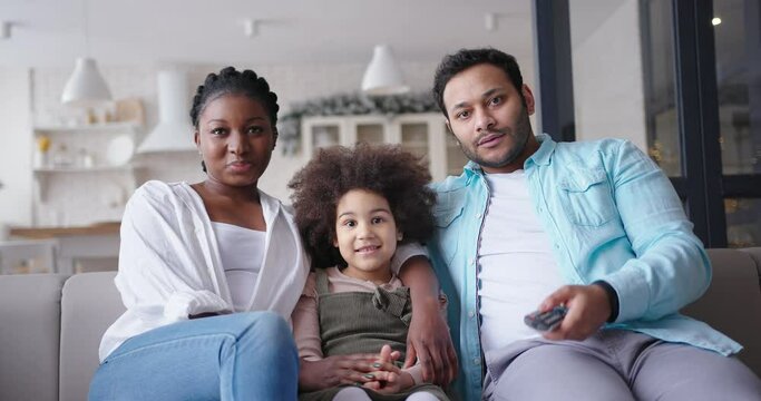 Happy young family hugs on sofa watching TV in living room