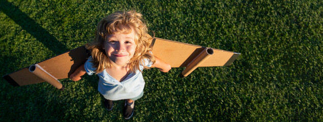 Banner with spring kids portrait. Funny child boy flying in plane made craft of cardboard wings....