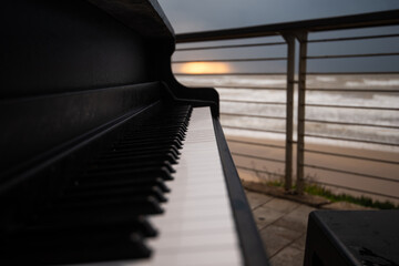 Piano outdoors in front of stormy sea at sunset time.