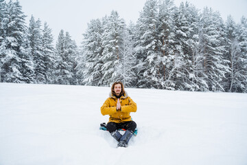 Fototapeta na wymiar A happy man rejoices in the snowfall. A man sits in the snow.Meditation. Panoramic view of the forest. A walk in the forest in winter