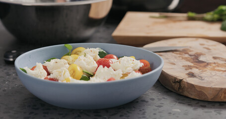 Closeup making salad with spinach, tomatoes and mozzarella in ablue bowl on concrete countertop