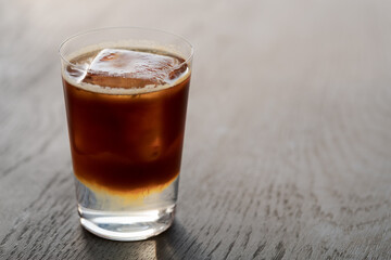 Espresso tonic with clear ice cube in tumbler glass on oak wood table with copy space