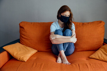 beautiful woman sitting on the orange sofa at home in protective masks Quarantine