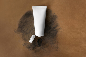 Top view blank label facial skincare white tube bottle with lid open product squeezed charcoal detox deep purifying creamy clay mask smear on eco friendly recyclable brown paper bag texture background