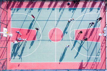 Young adult people play basketball at court. Men play streetball at outdoor court top down aerial...