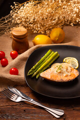 Salmon steaks topped with lemon sauce and asparagus in black dish on wood table.