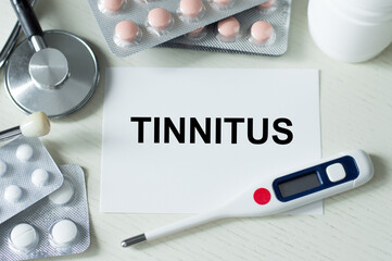 On the card text TINNITUS on the table next to it lies a stethoscope, thermometer, pills