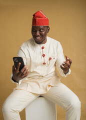 Yoruba Culturally Dressed Business Man Sitting with Phone in Hand Excited