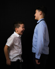 Two boys on a black background are brothers.Senior and junior.Atelier.The younger one is laughing at the older brother
