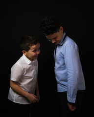 Two boys on a black background are brothers.Senior and junior.Atelier.they look at the floor.hands in pockets