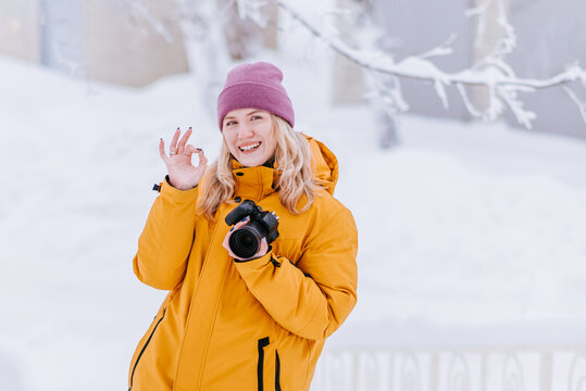 Smiling girl photographer taking pictures of snow in winter park