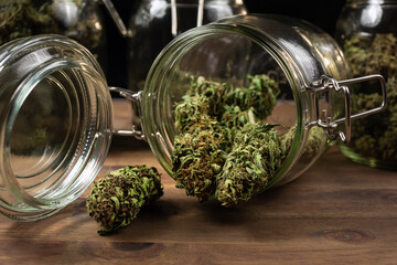 Dried cannabis hemp buds spill out of a glass jar, ready for consumption.