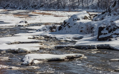 Fast river, rocks, ice, snow, trees, shrubs, dry grass in spring