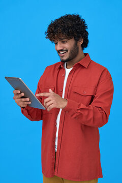 Happy Indian Young Man Using Digital Tablet Isolated On Blue Background. Smiling Ethnic Hipster Guy Holding Pad Playing Game In App, Buying Online In Ecommerce Store, Reading Ebook. Vertical