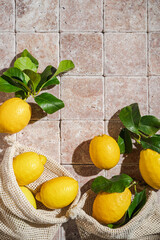 fresh organic sicilian lemons with green leaves in Cotton bag on natural stone tile background, sunny light with shadows flat lay, top view. Eco friendly zero waste shopping. co2 neutral gardening