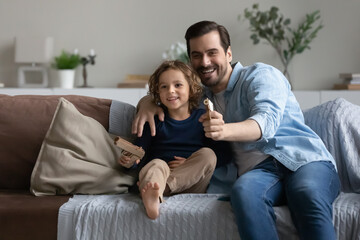 Fototapeta premium Father and son play toy guns shooting sit on sofa at home. Family spend free leisure time together, enjoy playtime. Boyish games of daddy and kid boy, pistols lovers, hobby, parent teach child concept