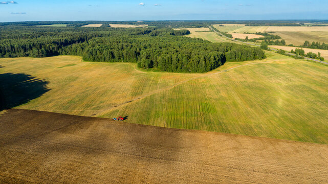 Scenic view of working tractor in the field agricultural field on a summer farm in the evening. Aerial photography, top view drone shot. Agricultural area of Moscow region. Agrarian land in summertime