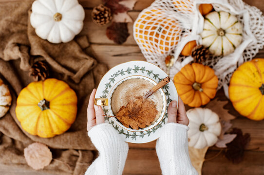 Womans Hands holding warm coffee with pumpkins and colorful leaves background top view. Stylish autumn flat lay. Hello fall. Cozy warm image