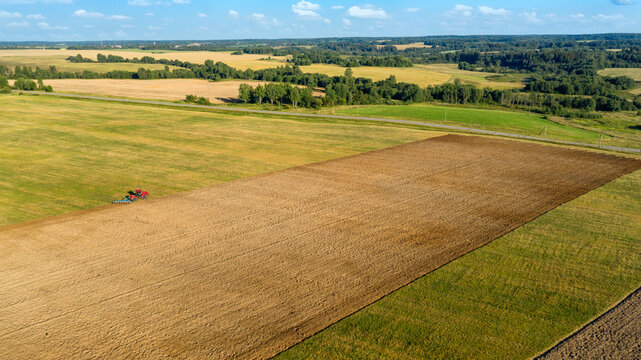 Scenic View Of Working Tractor In The Field Agricultural Field On A Summer Farm In The Evening. Aerial Photography, Top View Drone Shot. Agricultural Area Of Moscow Region. Agrarian Land In Summertime