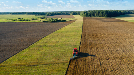 Scenic view of working tractor in the field agricultural field on a summer farm in the evening. Aerial photography, top view drone shot. Agricultural area of Moscow region. Agrarian land in summertime - obrazy, fototapety, plakaty