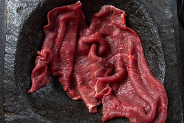 Raw beef fillet on black stone plate and mortar with herbs. Black background