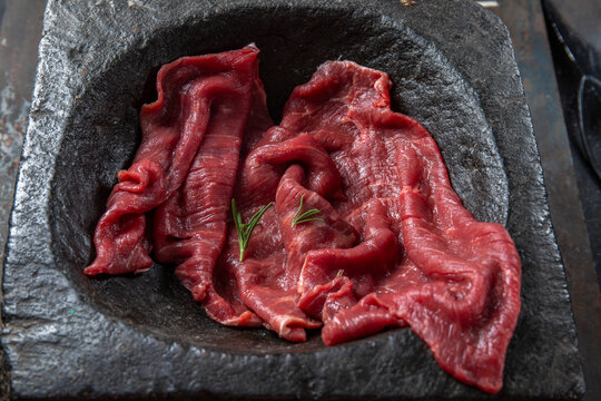 Raw beef fillet on black stone plate and mortar with herbs. Black background