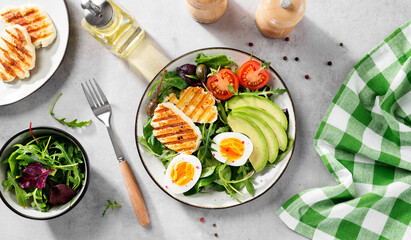 Healthy keto diet breakfast: boiled egg, avocado slices, grilled halloumi cheese, salad leaves. Light gray background. top view - 483713338