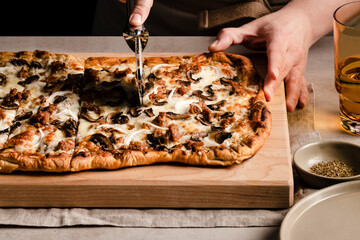 Hand slicing a mushroom, onion and sausage pizza on a cutting board.