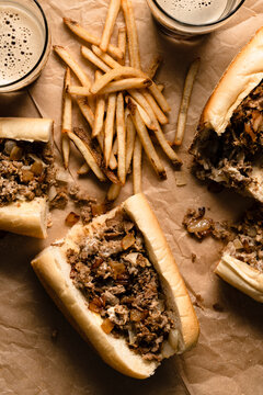 Cheesesteaks and fries on parchment paper with glasses of dark beer.