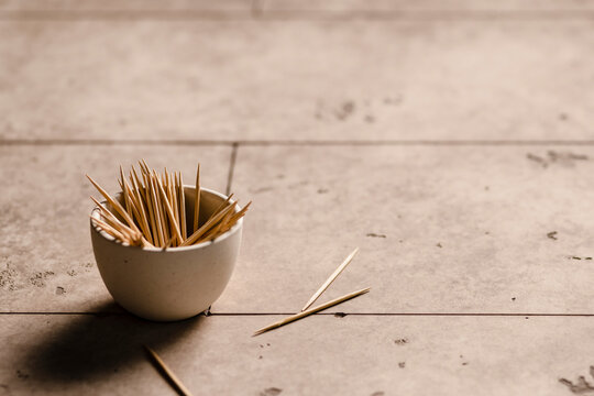 A small bowl of toothpicks on the edge of a table with a few scattered on the table.