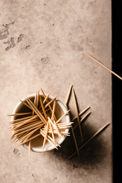 A small bowl of toothpicks on the edge of a table with a few scattered on the table.