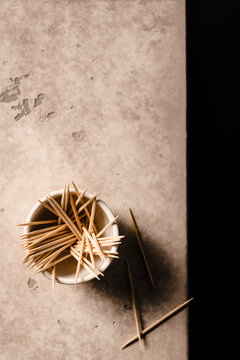A small bowl of toothpicks on the edge of a table with a few scattered on the table.