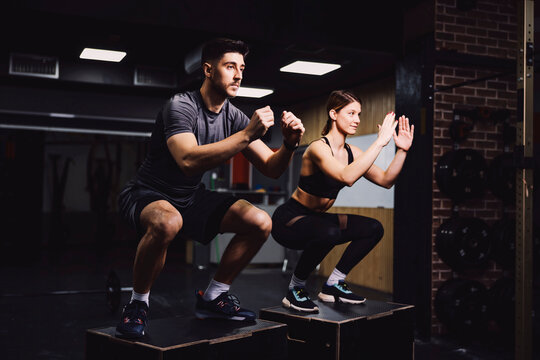 A dedicated sporty couple doing squats in a gym and practicing functional exercises.
