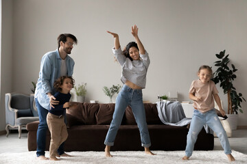 Untroubled family with little children dancing together in living room, full-length view, people...