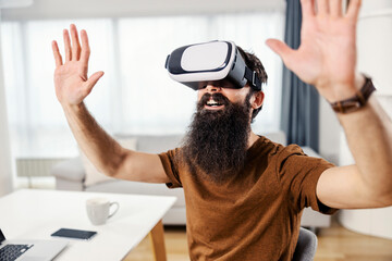A stunned bearded man sitting at his cozy home and having VR experience.
