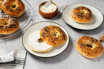 Fresh baked sourdough New York style bagels with cream cheese on light gray table.	