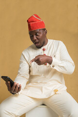 Yoruba Culturally Dressed Business Man Sitting with Phone in Hand Point at Info