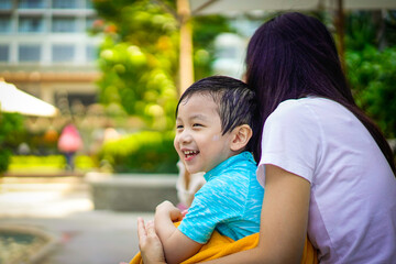A boy with smiling face sit with mother at the park. Mother and child sit together at the bench of swimming pool. Happy family  concept.