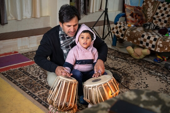 a small child learning to play the tabla from the teacher