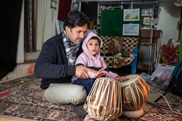 a small child learning to play the tabla from the teacher