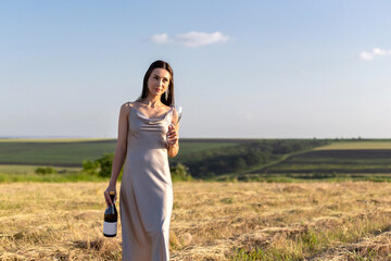 Happy girl with a bottle in her hands. On a field, at sunset.