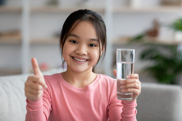 Positive chinese child with glass of water showing thumb up